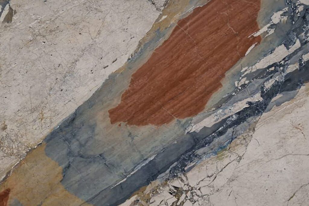 Mármol Breccia Vaticano natural con base clara y expresivos tonos rojizos, azules, grises y ocres, ideal para mesadas de baño, revestimientos y proyectos de interiorismo